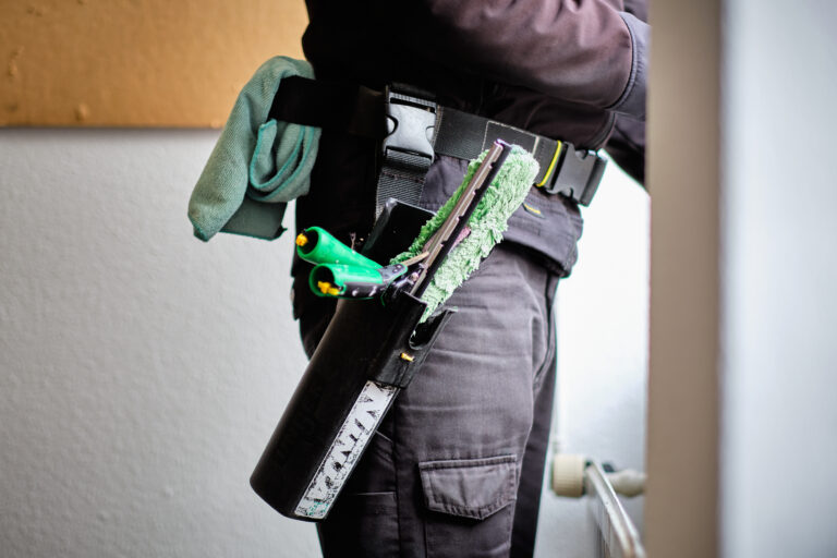 Close-up van een wisser in een houder, gedragen door een medewerker tijdens glasbewassing.